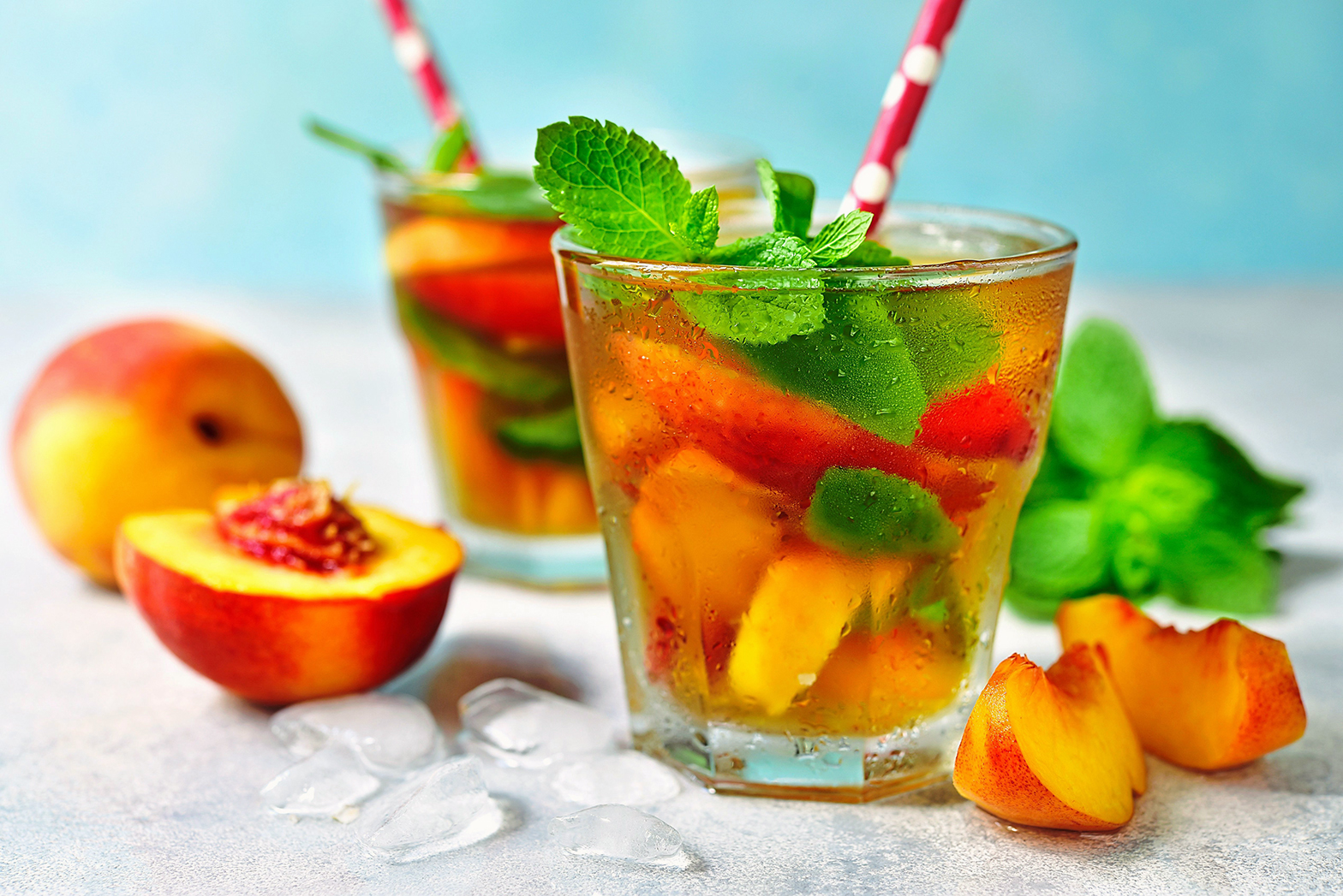 peach and mint iced black tea in two glasses with peaches around