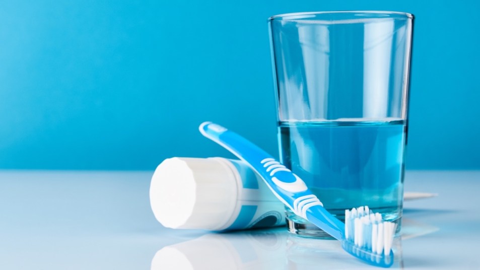 A cup of mouthwash, which should be used after brushing rather than before, next to a toothbrush and toothpase