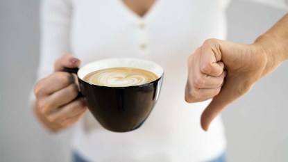 Woman doing a thumbs down gesture as she's holding a cup of coffee