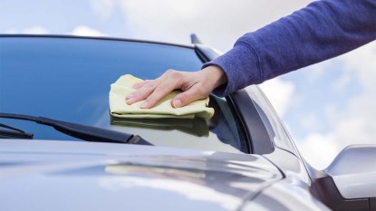 Womans-hand-with-rag-cleaning-a-silver-cars-windshield-on-cloudy-sky-background-in-sunny-day