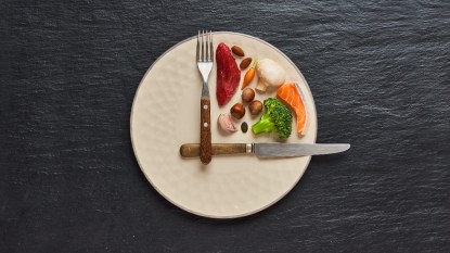 intermittent fasting concept, food on a plate with fork and knife marking a clock quarter