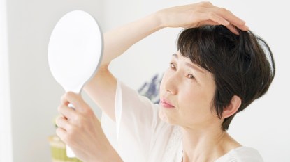 Asian middle aged woman checking her hair with the mirror at home