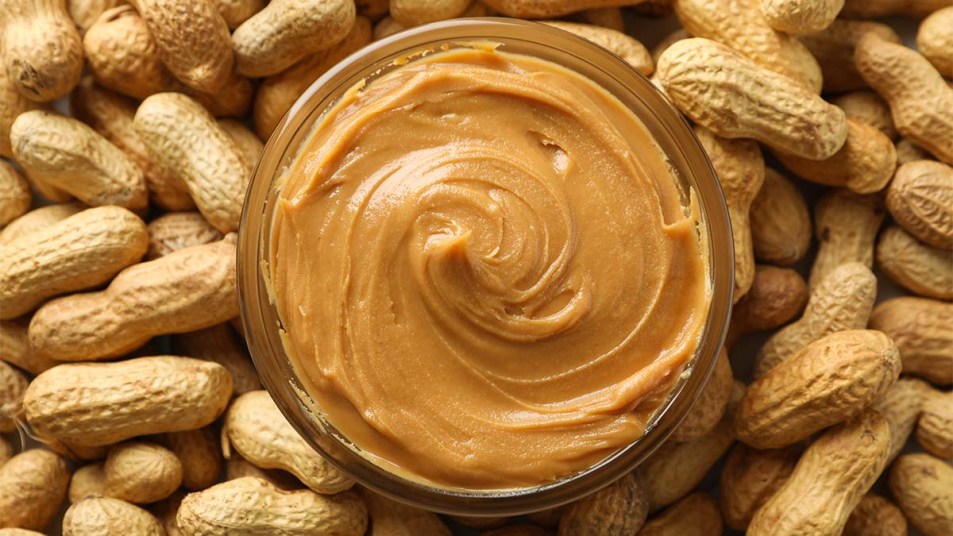 Jar with peanut butter on peanut background