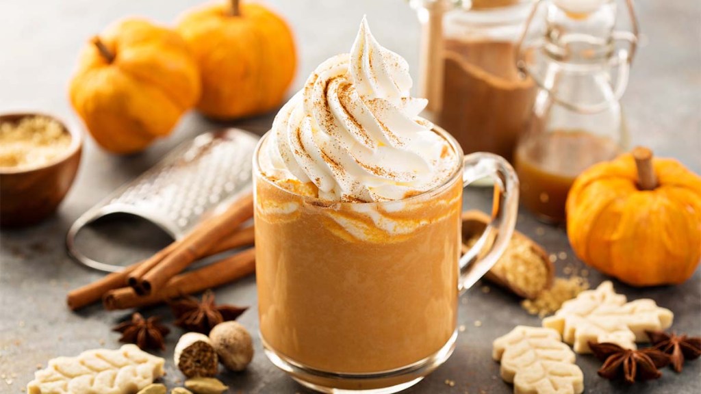 Pumpkin spice latte in a glass mug with cinnamon, nutmeg, and cookies