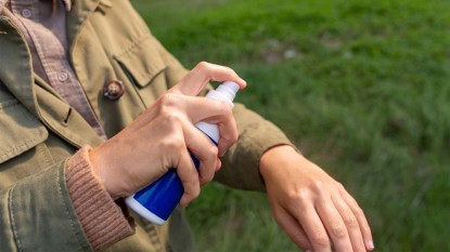 Woman spraying insect repellent or bug spray to her hand at park