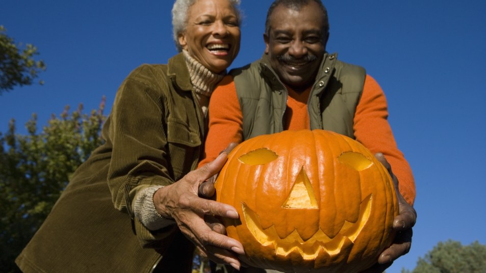 mature couple laughing and holding a pumpkin jack o lantern for pumpkin bowling