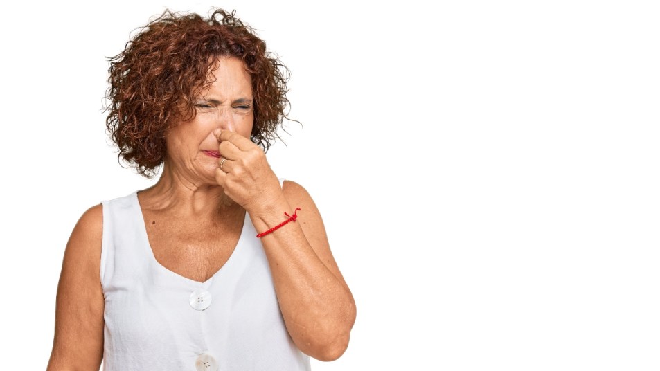 mature woman holding her nose and making a face from bad breath