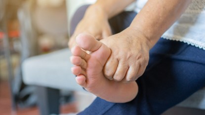 mature woman rubbing her foot, experiencing foot pain