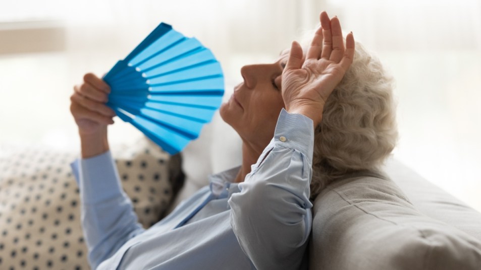 mature woman fanning herself from a hot flash post menopause