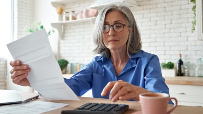 mature woman in blue shirt using calculator to reduce daily expenses