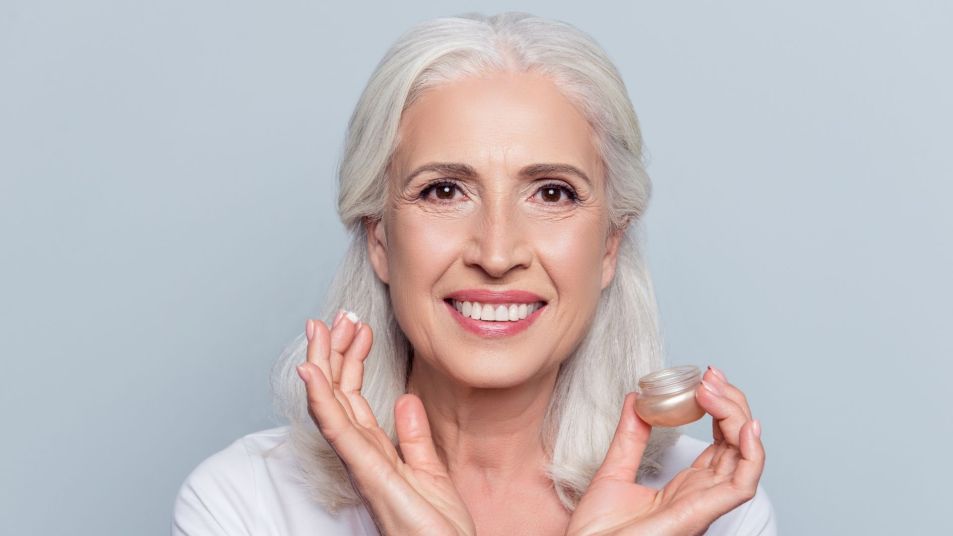 smiling mature woman applying popular anti-aging product to her face