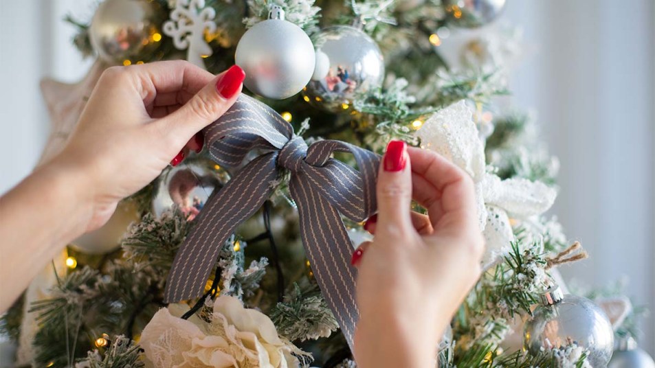 Woman putting ribbon on Christmas tree