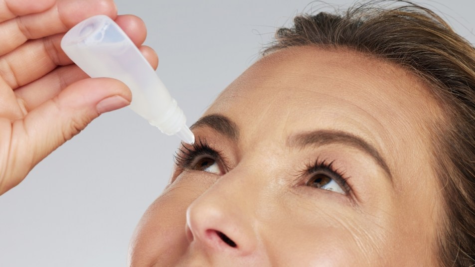 mature woman putting eye drops in her eye to replace reading glasses