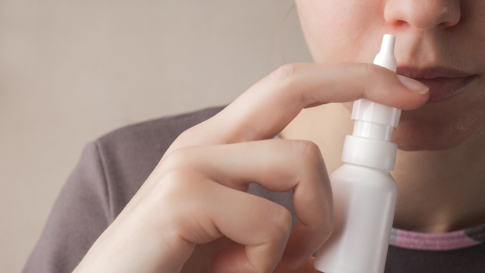 woman putting insulin nasal spray in her nose in plain white bottle