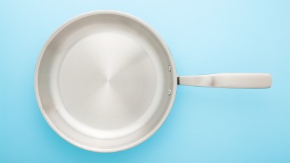 A stainless steel skillet against a blue background as part of a guide on fixing a warped pan