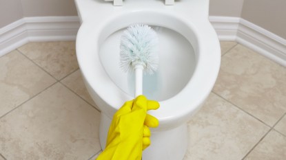 scrubbing a toilet bowl with a brush and yellow glove