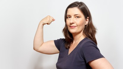 Middle aged woman flexing her biceps muscles, showing self-confidence and pride, white background