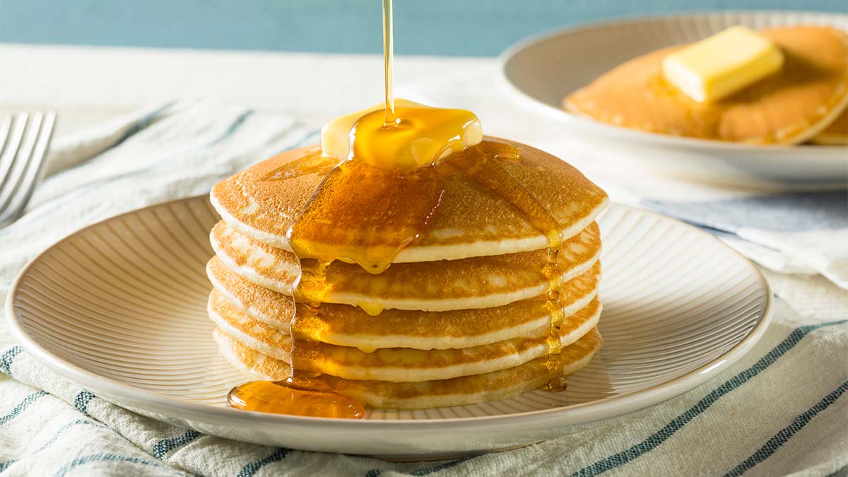 https://www.firstforwomen.com/wp-content/uploads/sites/2/2023/02/A-stack-of-pancakes-topped-with-butter-and-drizzled-with-syrup.jpg