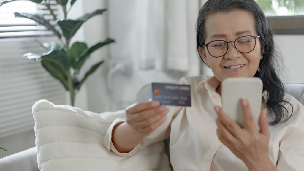 mature woman holding a credit card and looking at her phone