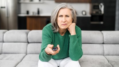 mature woman with a green sweater on a couch, looking confused, watching football