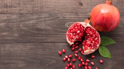 ripe pomegranate with seeds spilling onto wooden table
