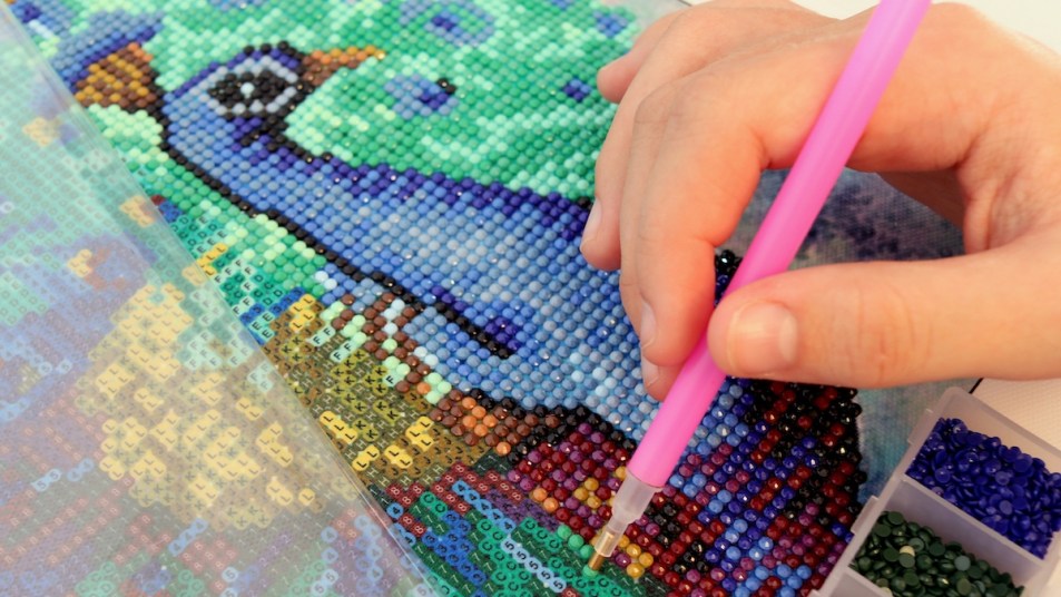 Woman's hand working on diamond art painting of peacock