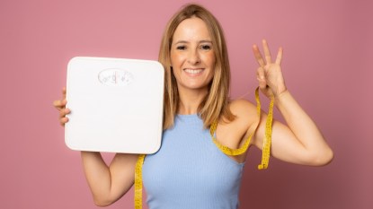 Young woman holding yellow measuring tape as dieting symbol and weight scales.