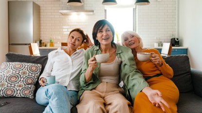 Three women sitting on couch and drinking tea while watching a movie