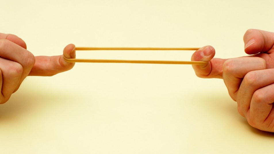 two hands stretching out a rubber band, holding by the index fingers, against a yellow background