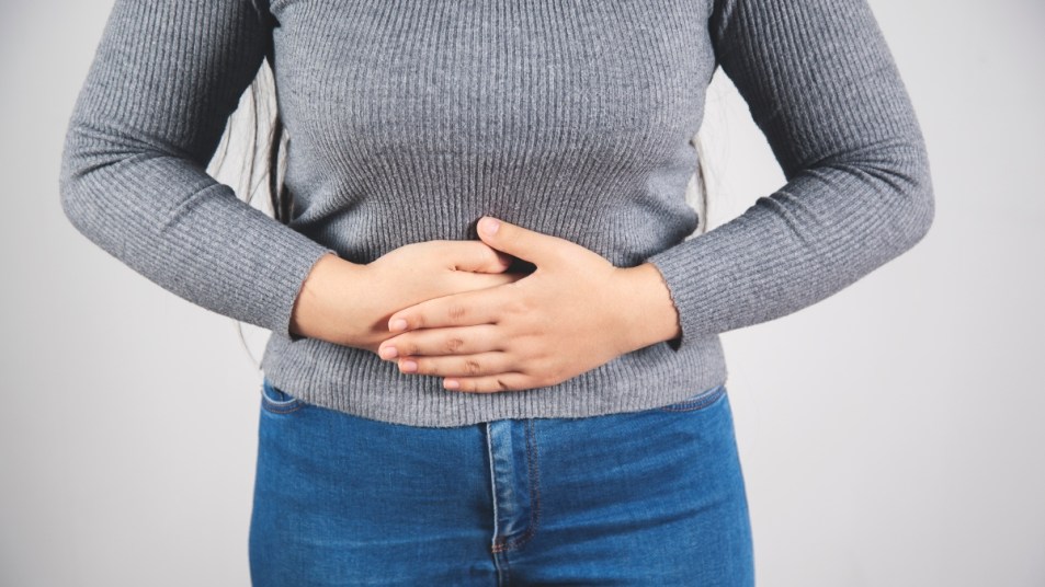 woman in gray sweater sucking in her stomach and holding it with her hands