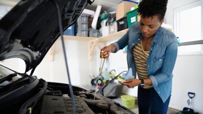 woman wearing a jean jacket doing an oil change on her car in the garage