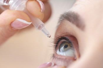 Woman drips eye drops into her eyes.