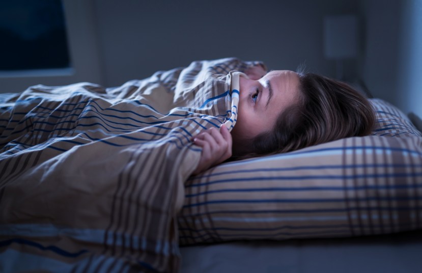 Woman with the covers pulled up under her nose, unable to sleep after nightmare