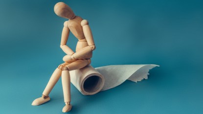 Wooden figure sit on a roll of toilet paper. Concept of the problem with digestion.