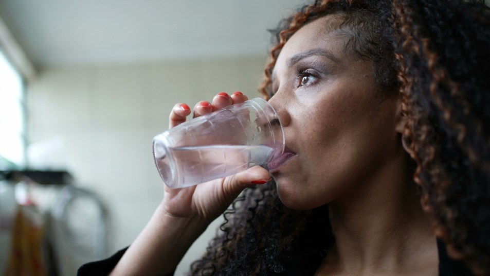 A pensive African American woman drinking water staying hydrated