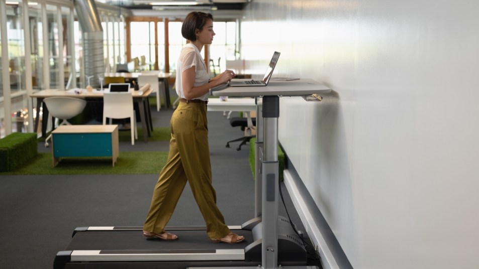 Businesswoman working on laptop while doing exercise on treadmill