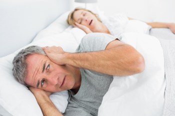 Fed up man blocking his ears from noise of wife snoring at home in bedroom