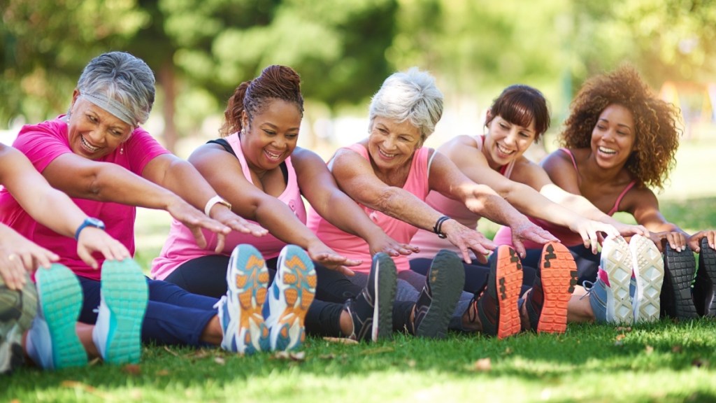 A group of women sitting in the grass reaching for their toes while exercising and stretching