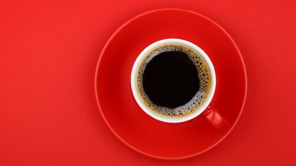 A red coffee mug filled with coffee set on a red background