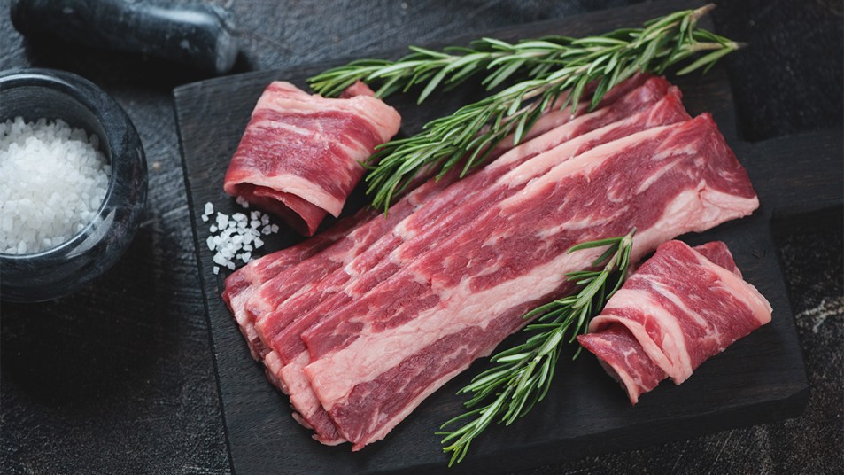 Raw marbled beef bacon with fresh rosemary and salt on a black wooden chopping board