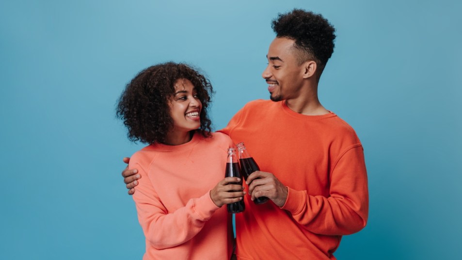 Man and woman clinking soda bottles on a blue background