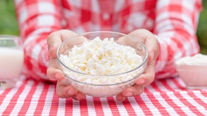 Woman's hands holding bowl of cottage cheese on gingham tablecloth