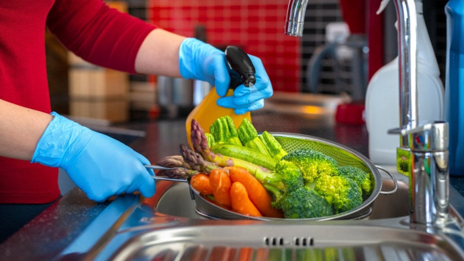 woman spraying vegetables in a sink with a sprayer, concept for hydrogen peroxide