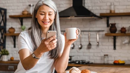 Woman happily looking at her phone as she drinks coffee