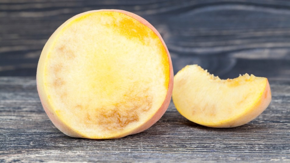 cut ripe peach with traces inside rot and decay, close-up of fruit on cutting board