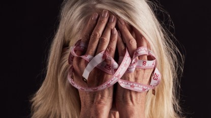 mature woman stressed with measuring tape and hands over face