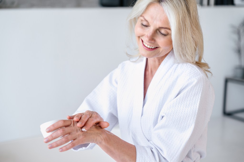 Blond woman in a white robe applying lotion to relieve her dry, cracked hands