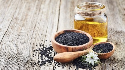 Black cumin oil with seeds and flower nigella sativa on wooden background