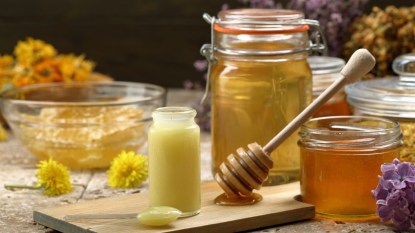 A vial of royal jelly next to containers of honey