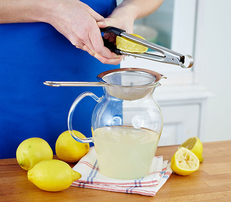 Woman using tongs to squeeze juice out of a fresh lemon